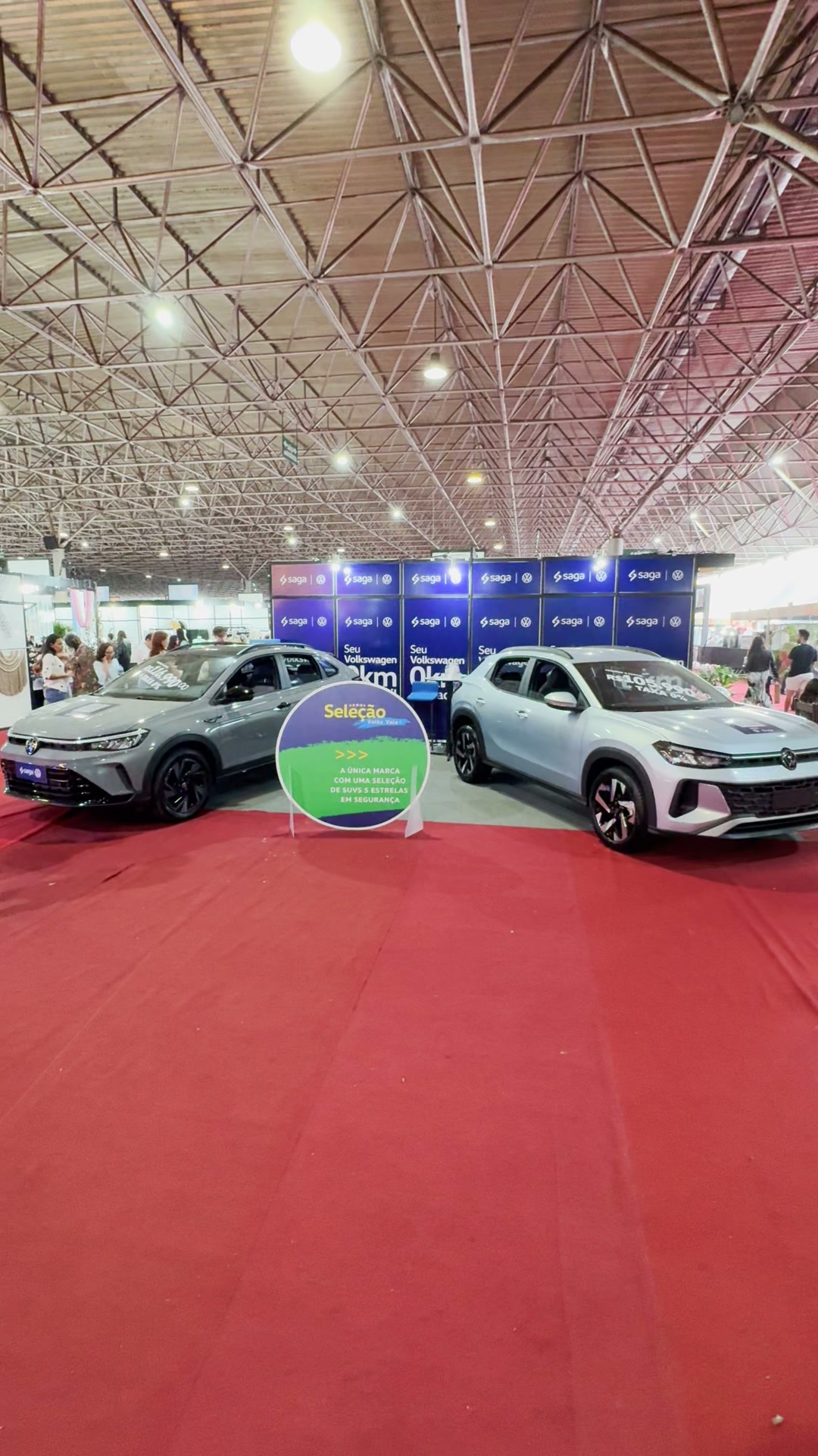 Estande da Volkswagen na Expotchê: dois veículos sobre tapete vermelho diante do painel da concessionária Saga.